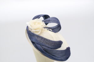 Ivory sinamay fascinator base with navy ribbon swirls looped around the fascinator and an ivory silk rose