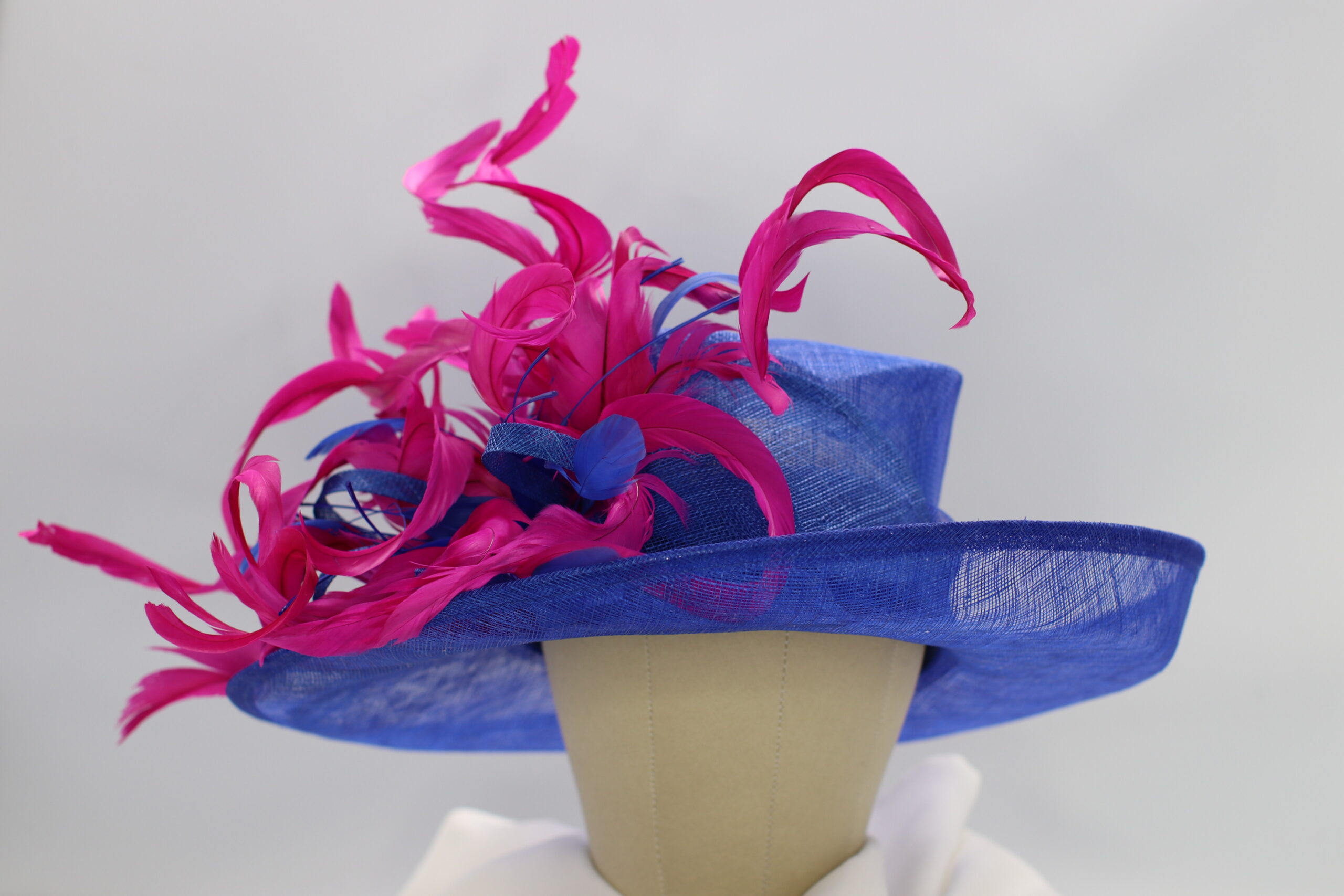 Royal blue sinamay hat decorated with dramatic, hot pink, and curled feathers
