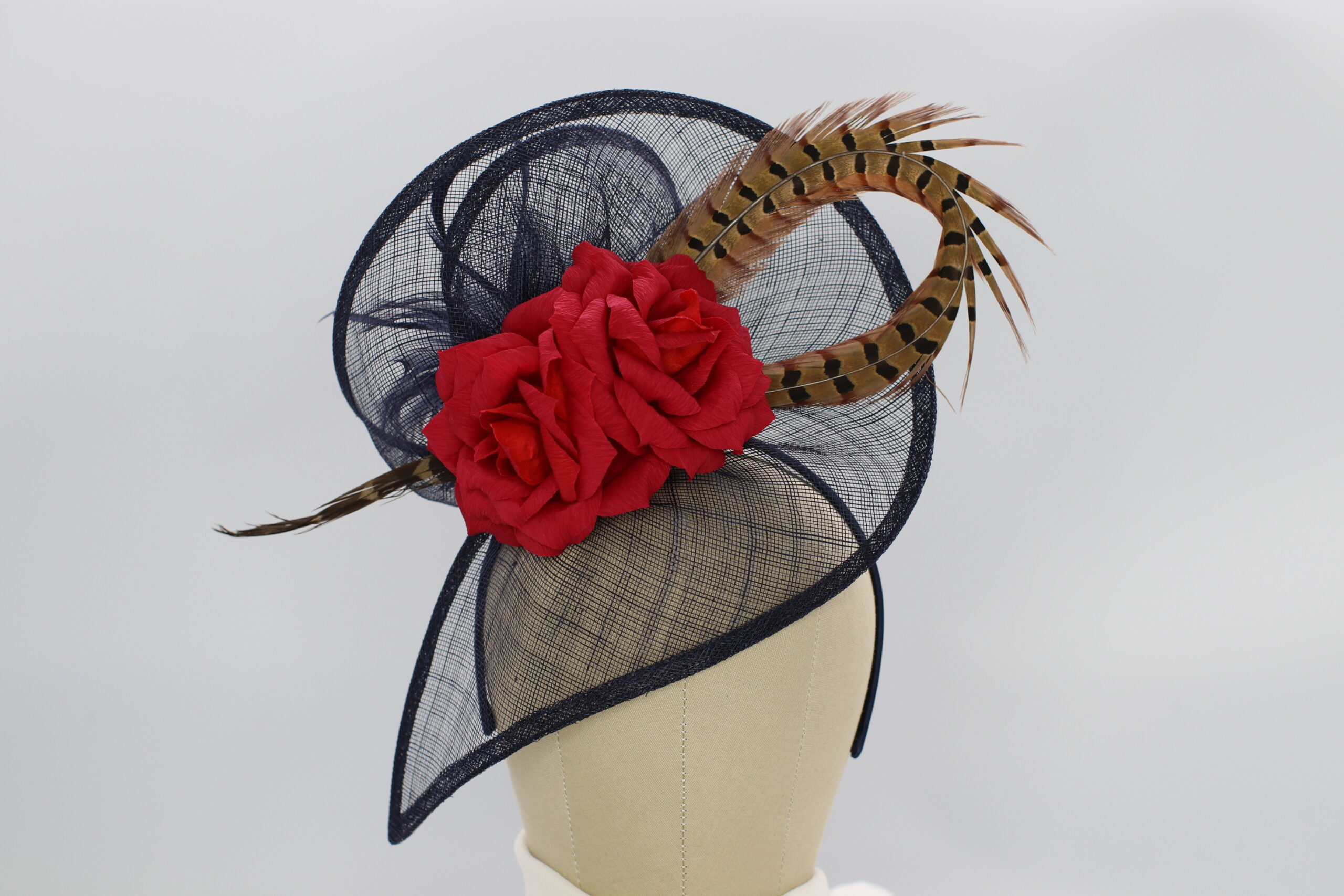 Navy blue fascinator with a pheasant feather and two hand-crafted red roses. Attached with a satin headband.